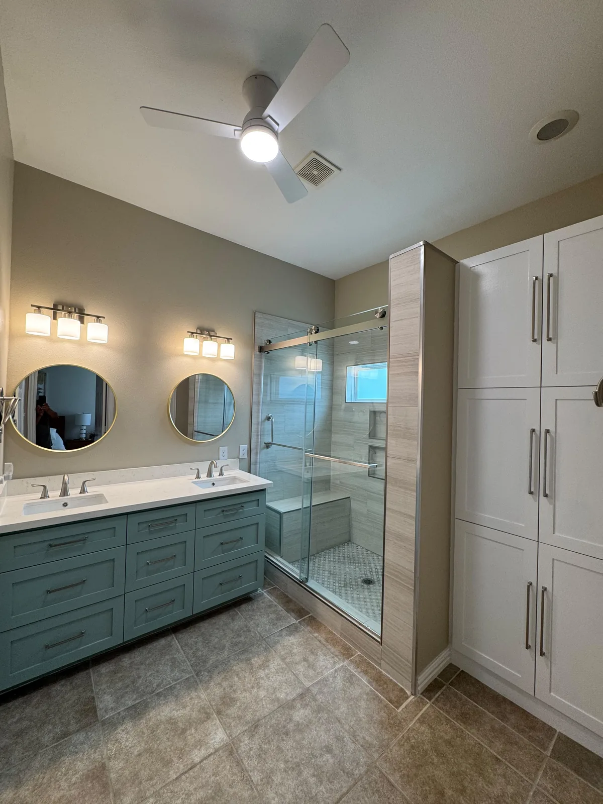 A Houston master bathroom refreshed with a teal vanity, round mirrors and a walk in shower after the remodel